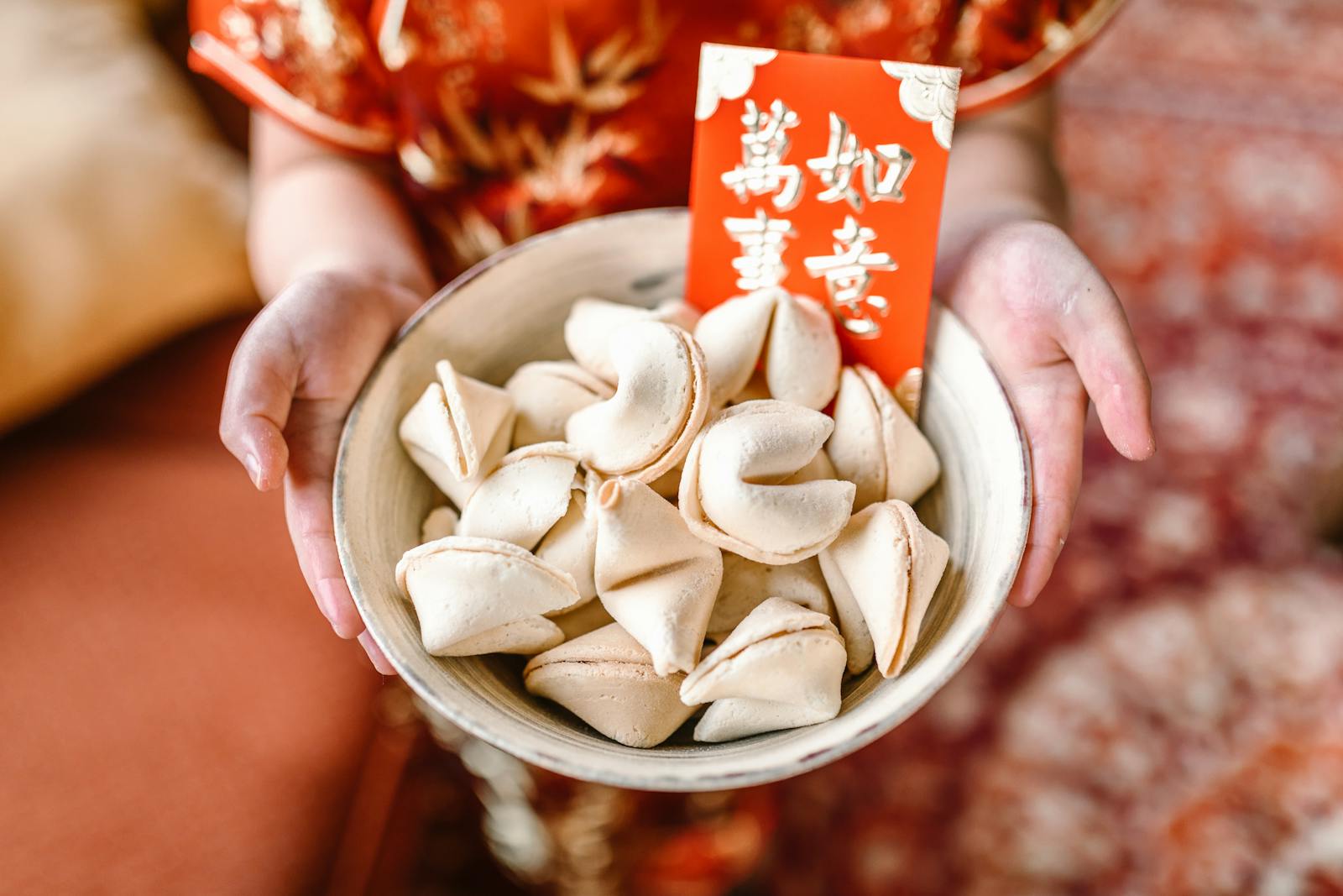 A set of fortune cookies in a bowl held by hands, accompanied by a red envelope, symbolizes Chinese New Year celebrations.